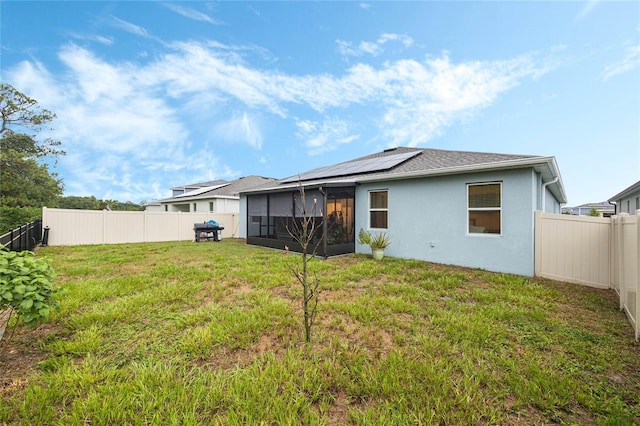 rear view of property with a sunroom, a lawn, and solar panels