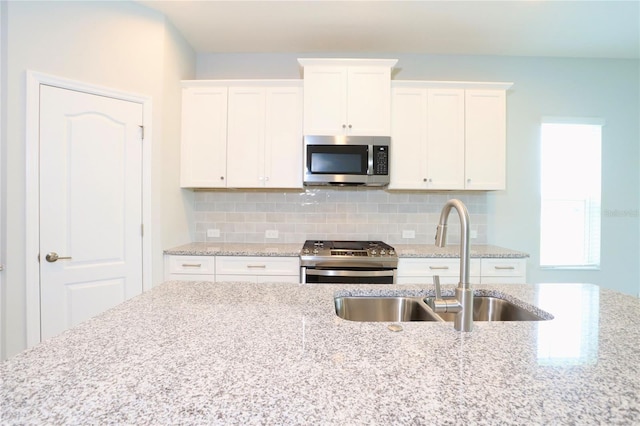 kitchen with appliances with stainless steel finishes, light stone counters, backsplash, and sink