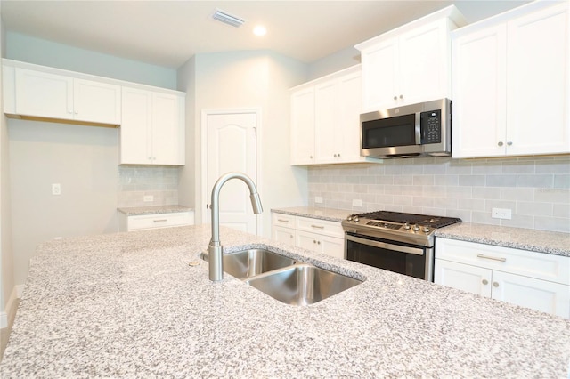 kitchen featuring light stone countertops, appliances with stainless steel finishes, sink, decorative backsplash, and white cabinets