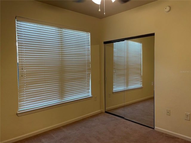 unfurnished bedroom featuring carpet floors, ceiling fan, multiple windows, and a closet