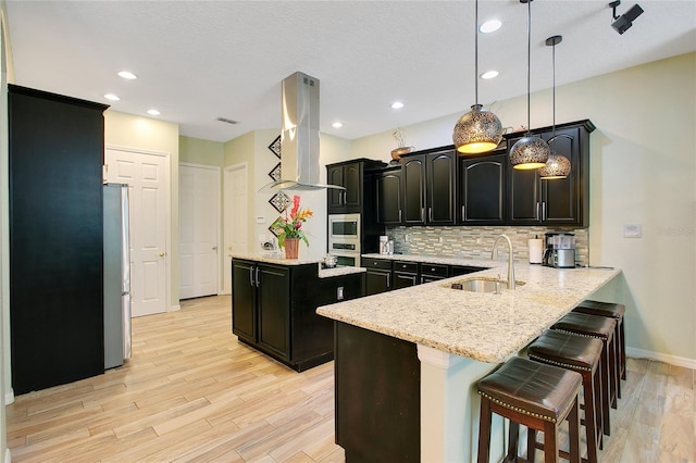 kitchen featuring island range hood, dark cabinets, a peninsula, stainless steel appliances, and a sink