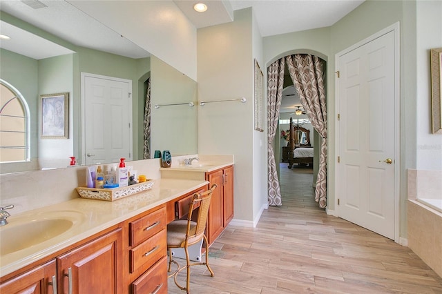 full bath with ensuite bathroom, a relaxing tiled tub, a sink, wood finished floors, and double vanity