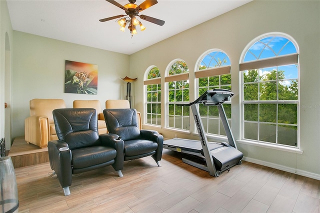 workout room featuring a ceiling fan, arched walkways, baseboards, and light wood finished floors