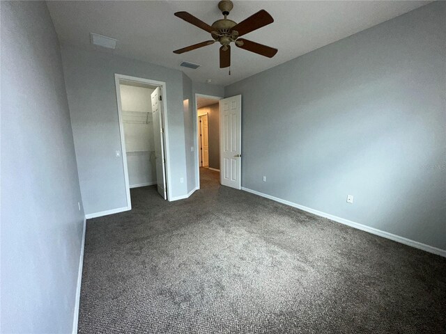 unfurnished bedroom with ceiling fan, a spacious closet, dark carpet, and a closet