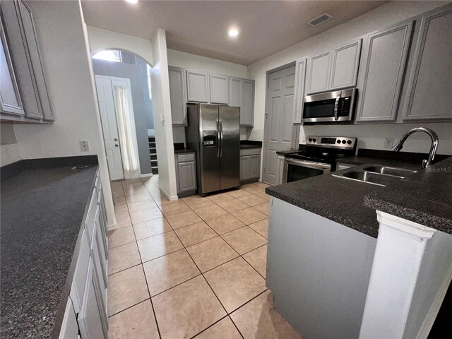 kitchen with appliances with stainless steel finishes, light tile patterned floors, gray cabinets, and sink