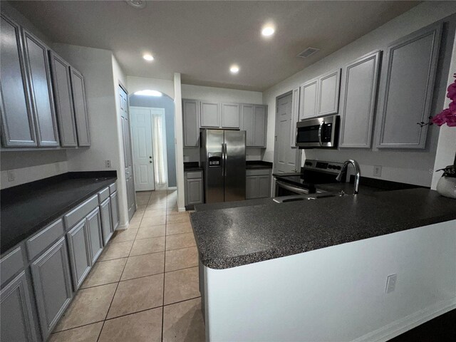 kitchen featuring stainless steel appliances, sink, gray cabinetry, light tile patterned floors, and kitchen peninsula