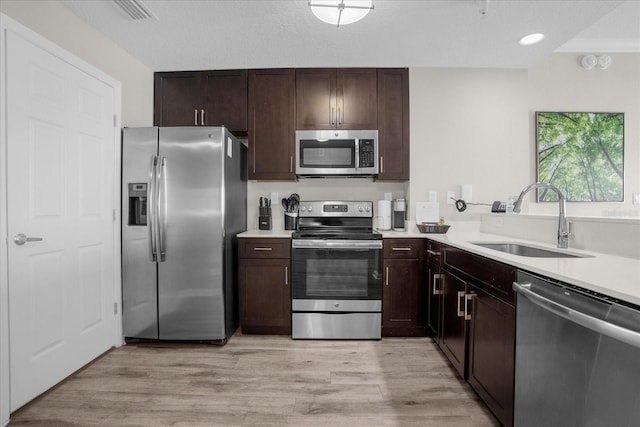 kitchen with appliances with stainless steel finishes, light wood-style floors, light countertops, and a sink