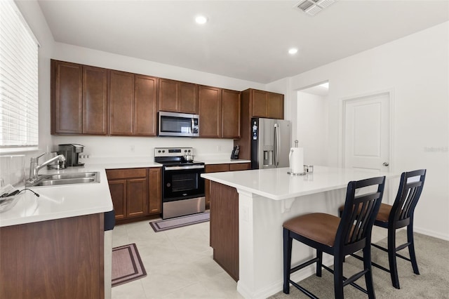 kitchen featuring light tile patterned floors, stainless steel appliances, sink, a breakfast bar area, and a kitchen island