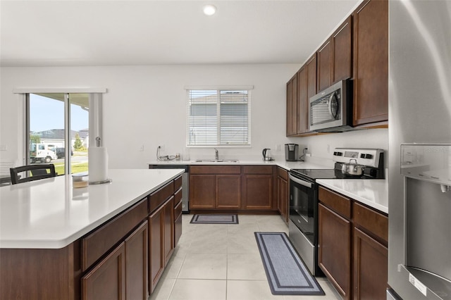 kitchen with stainless steel appliances, dark brown cabinets, light tile patterned flooring, and sink