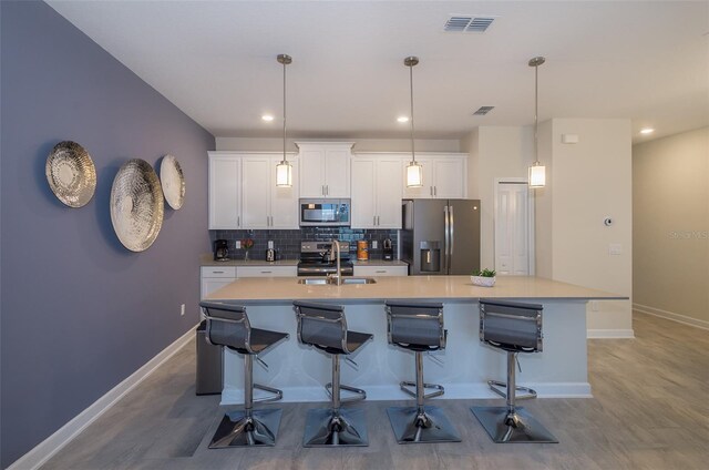 kitchen featuring decorative backsplash, light hardwood / wood-style flooring, a center island with sink, and stainless steel appliances