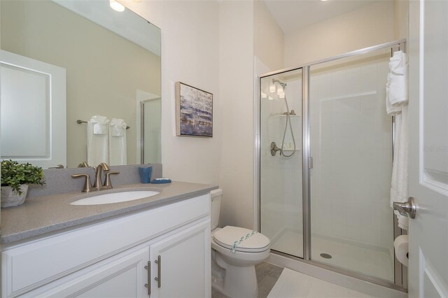 bathroom featuring a shower with door, vanity, and toilet