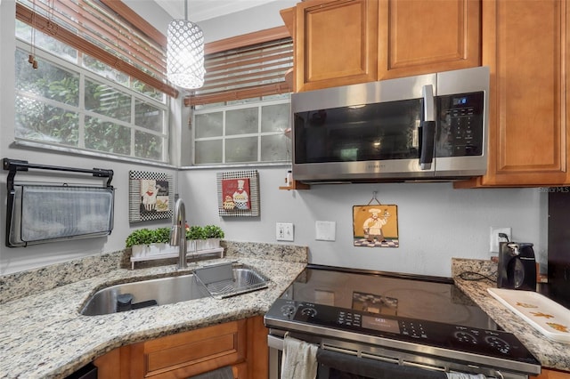 kitchen with appliances with stainless steel finishes, decorative light fixtures, sink, and light stone countertops