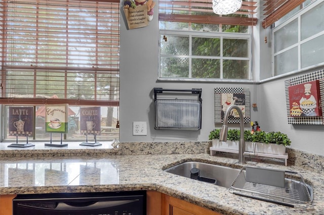 kitchen with dishwashing machine, light stone counters, and sink