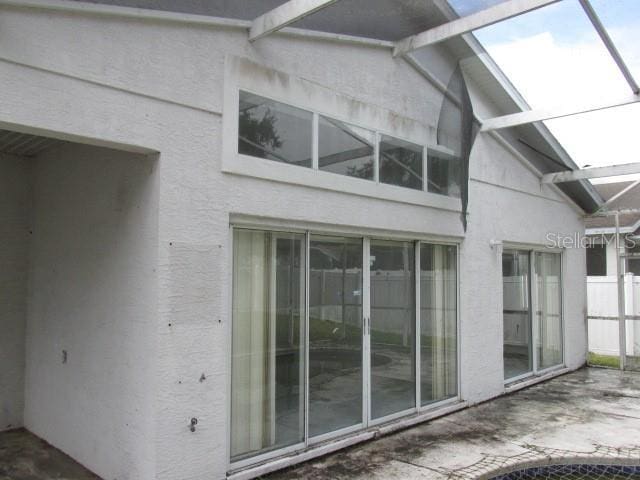 view of side of property featuring glass enclosure, a patio area, and stucco siding