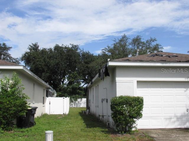 view of side of home featuring an attached garage, stucco siding, fence, and a yard