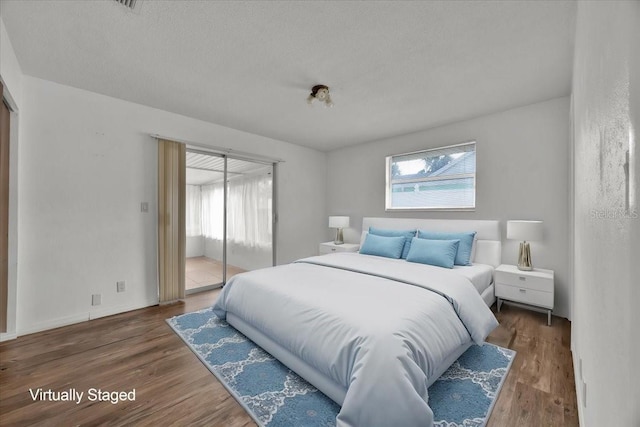 bedroom with a textured ceiling, dark wood-style flooring, and access to exterior