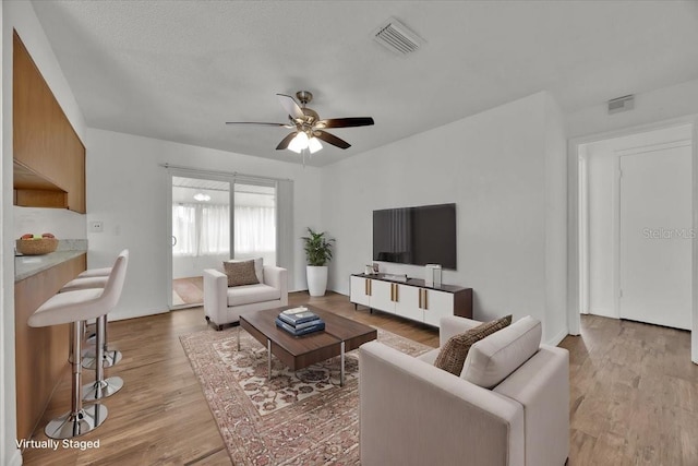 living area with light wood-style floors, visible vents, and ceiling fan