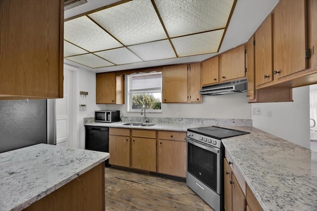 kitchen with dark wood-style floors, appliances with stainless steel finishes, brown cabinets, under cabinet range hood, and a sink