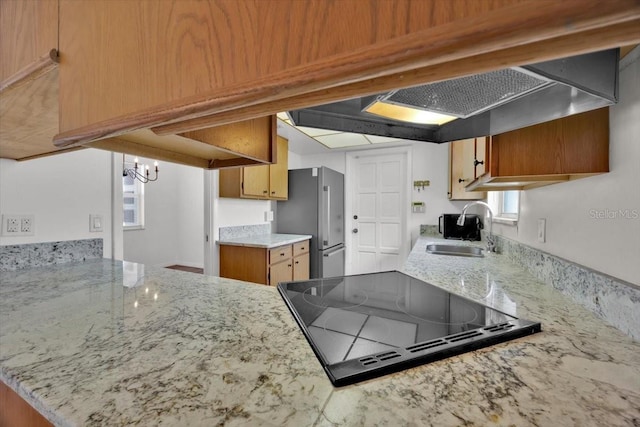 kitchen featuring brown cabinetry, stove, freestanding refrigerator, a sink, and a notable chandelier