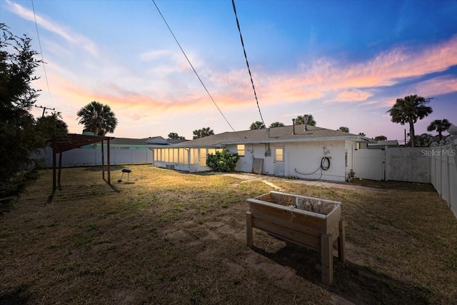 back of property at dusk with a lawn, a fenced backyard, and a gate