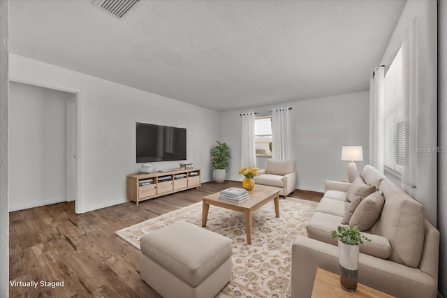 living room featuring a textured ceiling, wood finished floors, visible vents, and baseboards