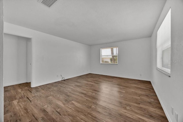 empty room with visible vents, a textured ceiling, baseboards, and wood finished floors