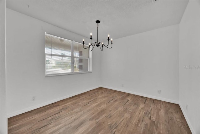 unfurnished room with baseboards, a textured ceiling, a chandelier, and wood finished floors