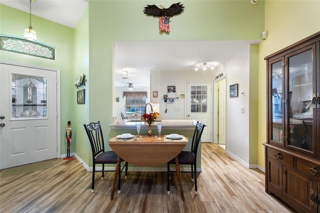 dining room with baseboards, light wood-style floors, a towering ceiling, and wallpapered walls