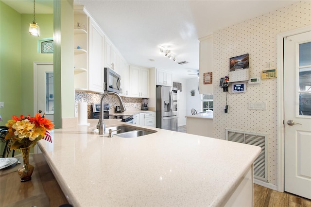 kitchen with white cabinets, decorative light fixtures, a peninsula, stainless steel appliances, and light countertops