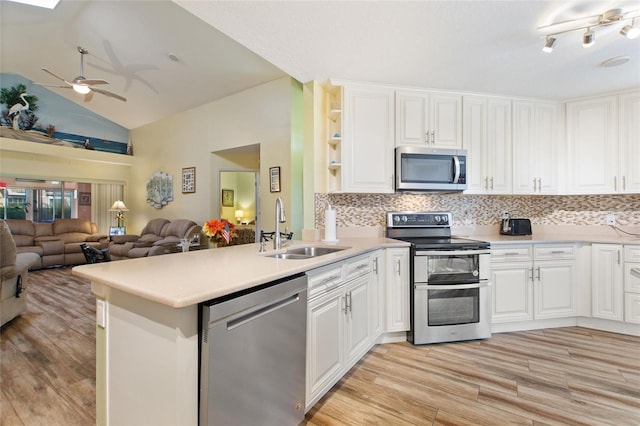 kitchen featuring a peninsula, a sink, white cabinets, open floor plan, and appliances with stainless steel finishes