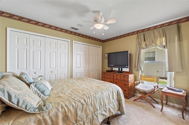 bedroom featuring light carpet, baseboards, visible vents, ceiling fan, and two closets