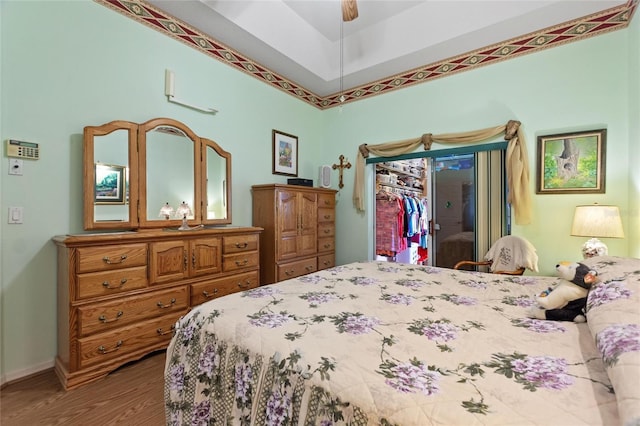 bedroom with a closet, a spacious closet, a ceiling fan, wood finished floors, and baseboards