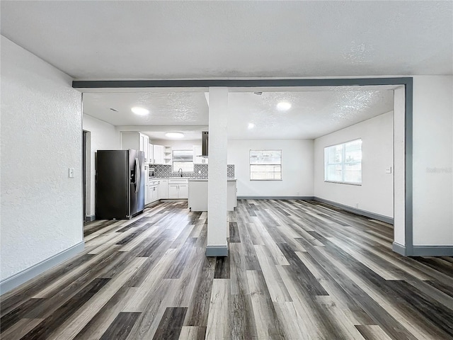 unfurnished living room with baseboards, a textured wall, dark wood-style flooring, a textured ceiling, and a sink