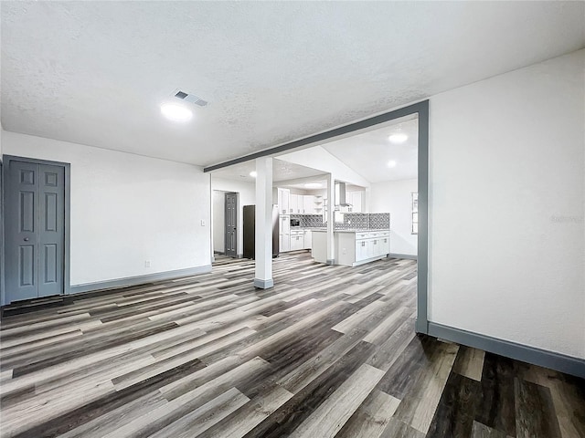 unfurnished living room with baseboards, a textured ceiling, visible vents, and wood finished floors