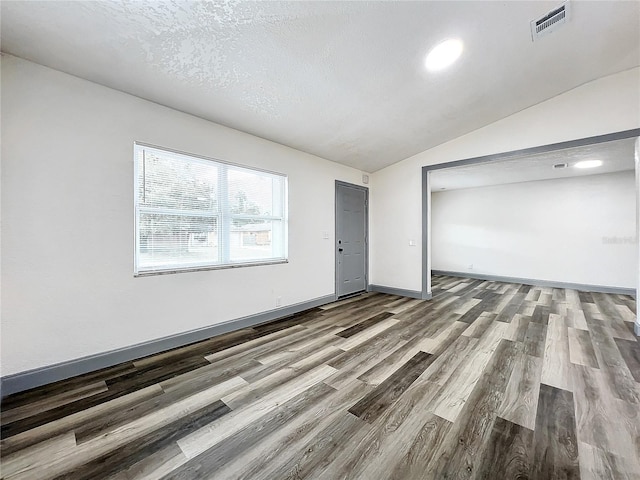 spare room with baseboards, visible vents, lofted ceiling, wood finished floors, and a textured ceiling