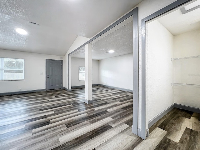 interior space with a textured ceiling, dark wood-style flooring, visible vents, and baseboards