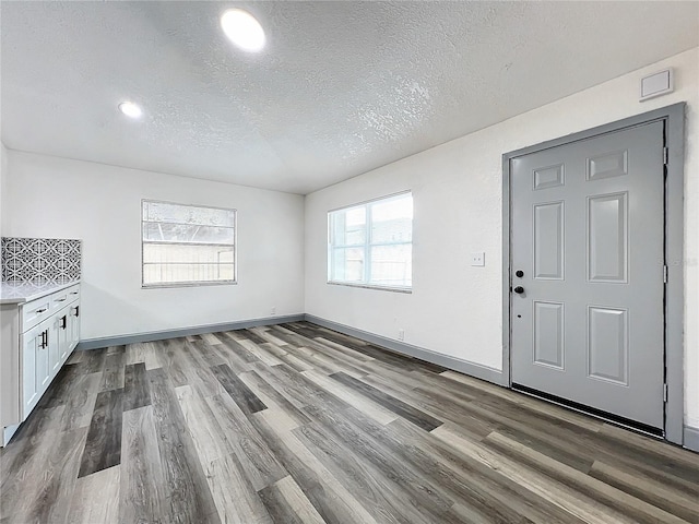 interior space with a textured ceiling, baseboards, and wood finished floors