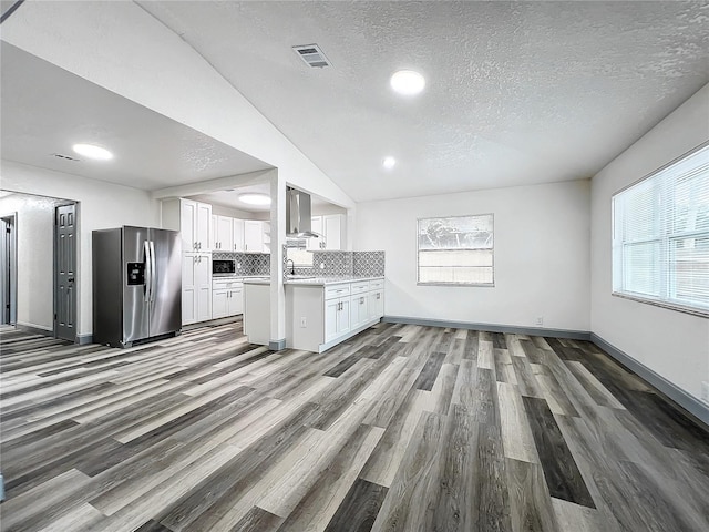 kitchen with stainless steel fridge with ice dispenser, light countertops, wall chimney range hood, white cabinetry, and backsplash