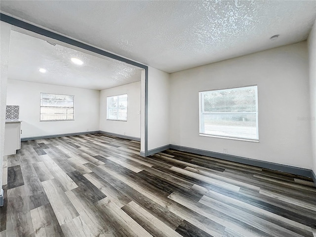 unfurnished room with dark wood-type flooring, a textured ceiling, and baseboards