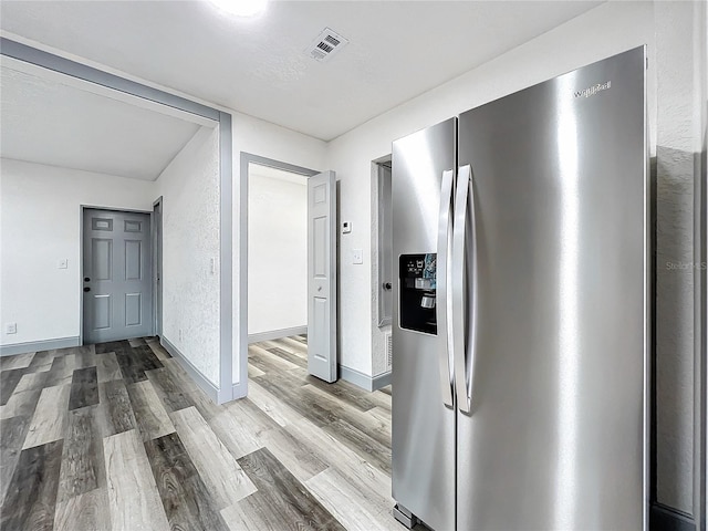 interior space with stainless steel refrigerator with ice dispenser, visible vents, a textured wall, light wood-style flooring, and baseboards