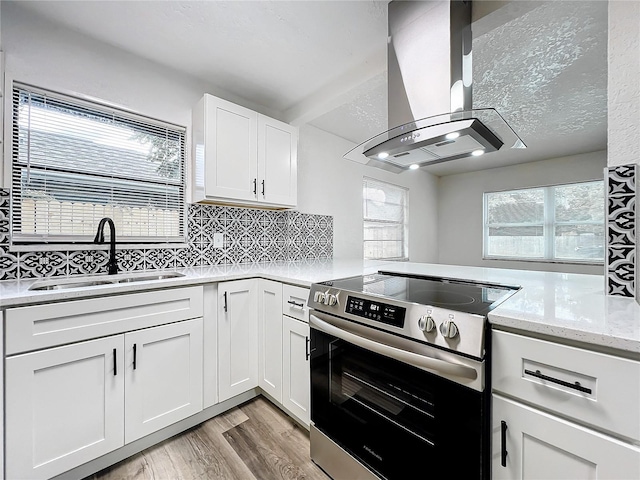 kitchen featuring electric range, a sink, white cabinets, light wood finished floors, and island exhaust hood