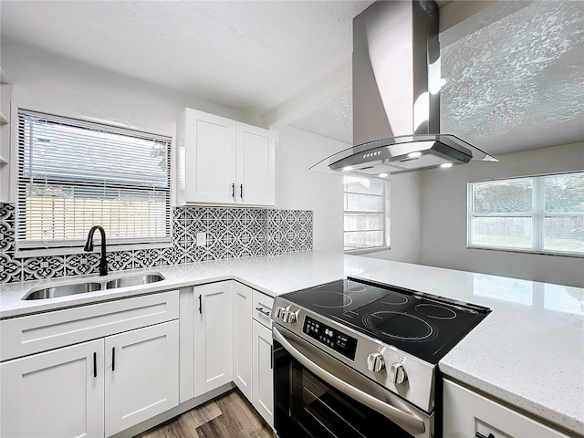 kitchen featuring stainless steel electric stove, tasteful backsplash, white cabinets, a sink, and island range hood