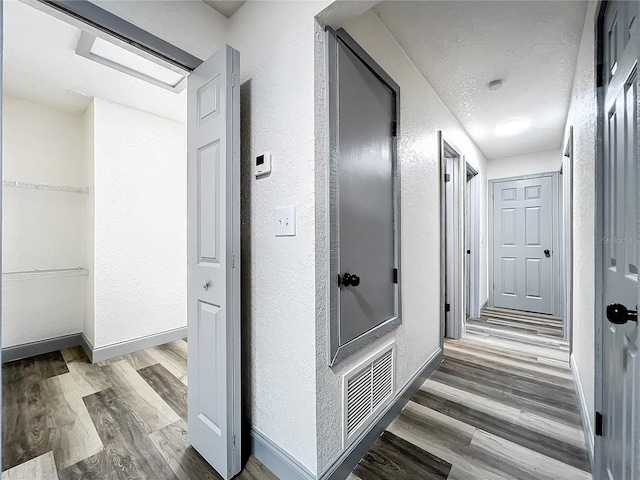 corridor featuring visible vents, a textured wall, a textured ceiling, wood finished floors, and baseboards