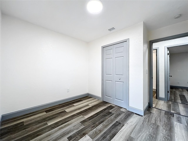 unfurnished bedroom featuring dark wood-type flooring, a closet, visible vents, and baseboards