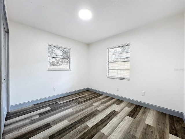 unfurnished room with a healthy amount of sunlight, dark wood finished floors, and baseboards