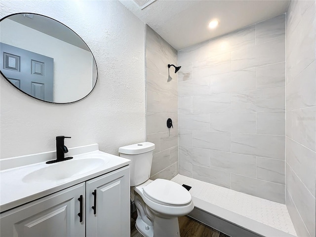 full bath featuring a shower stall, a textured wall, vanity, and toilet