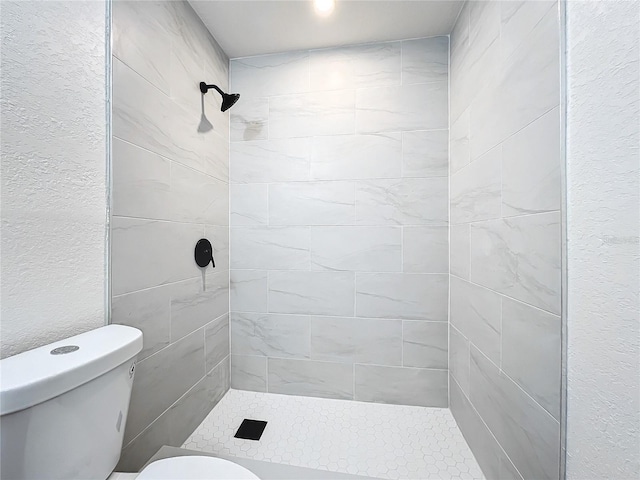 bathroom with a textured wall, a shower stall, and toilet