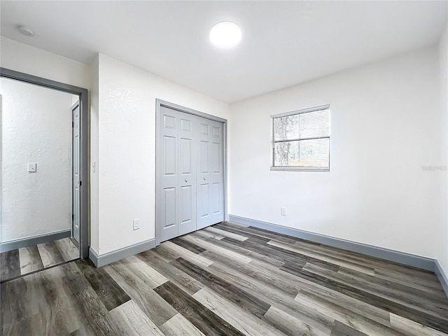 unfurnished bedroom with a closet, baseboards, and dark wood-style flooring