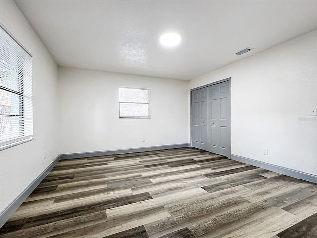 unfurnished bedroom featuring a closet, multiple windows, visible vents, and wood finished floors