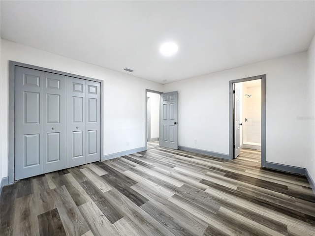 unfurnished bedroom with baseboards, visible vents, connected bathroom, wood finished floors, and a closet